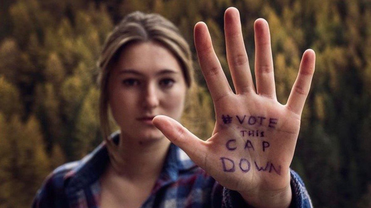 Camille Étienne montre le creux de sa main à l'objectif photo. Y est écrit : "#VotethisCAPdown"