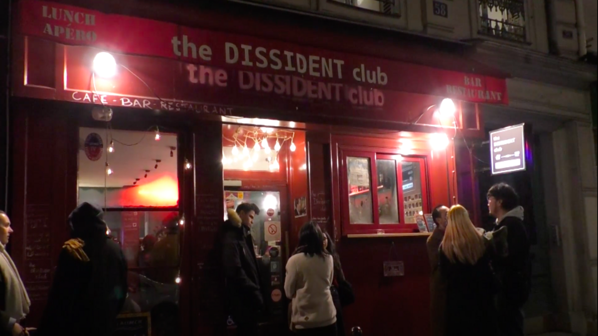 Devanture du Dissident Club de nuit à Paris. La devanture est rouge avec des lumières. Des personnes sont devant en train de discuter.
